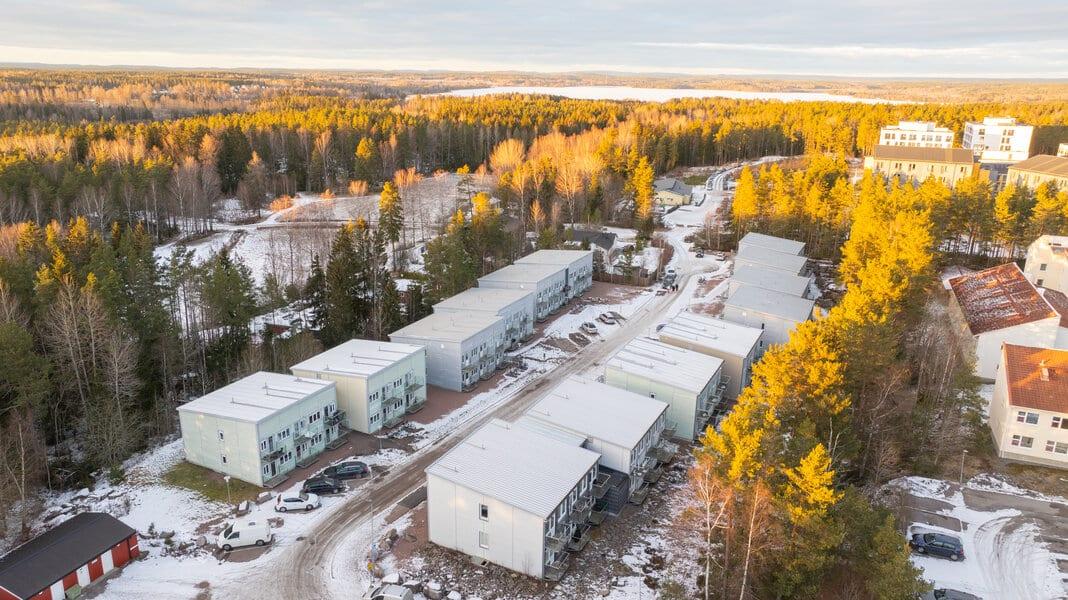 Trio Apartments sett från luften — husen längs gatan med skog och sjö bakom