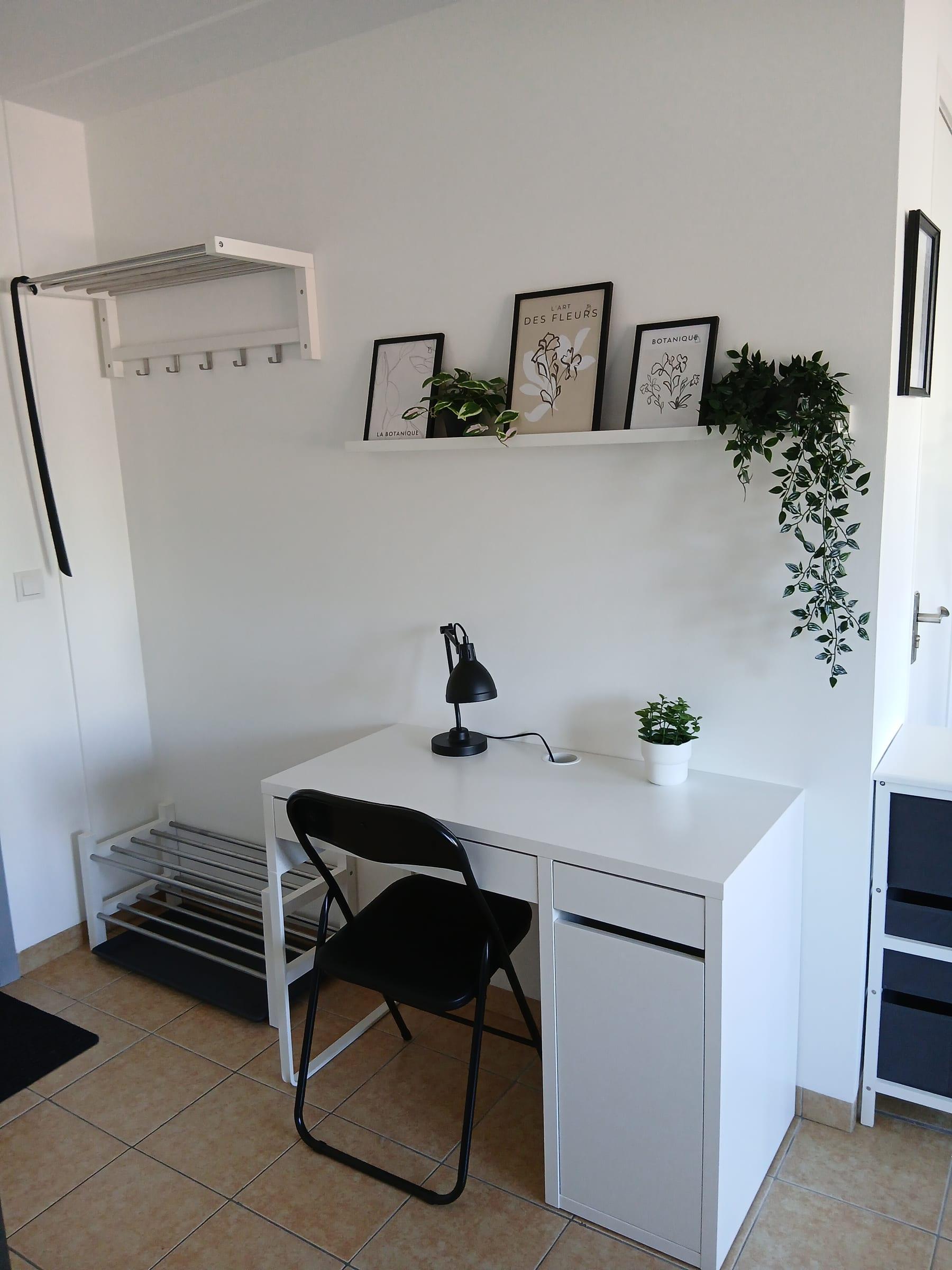 Arbetsplats med skrivbord, stol, bordslampa och hatthylla vid entrén