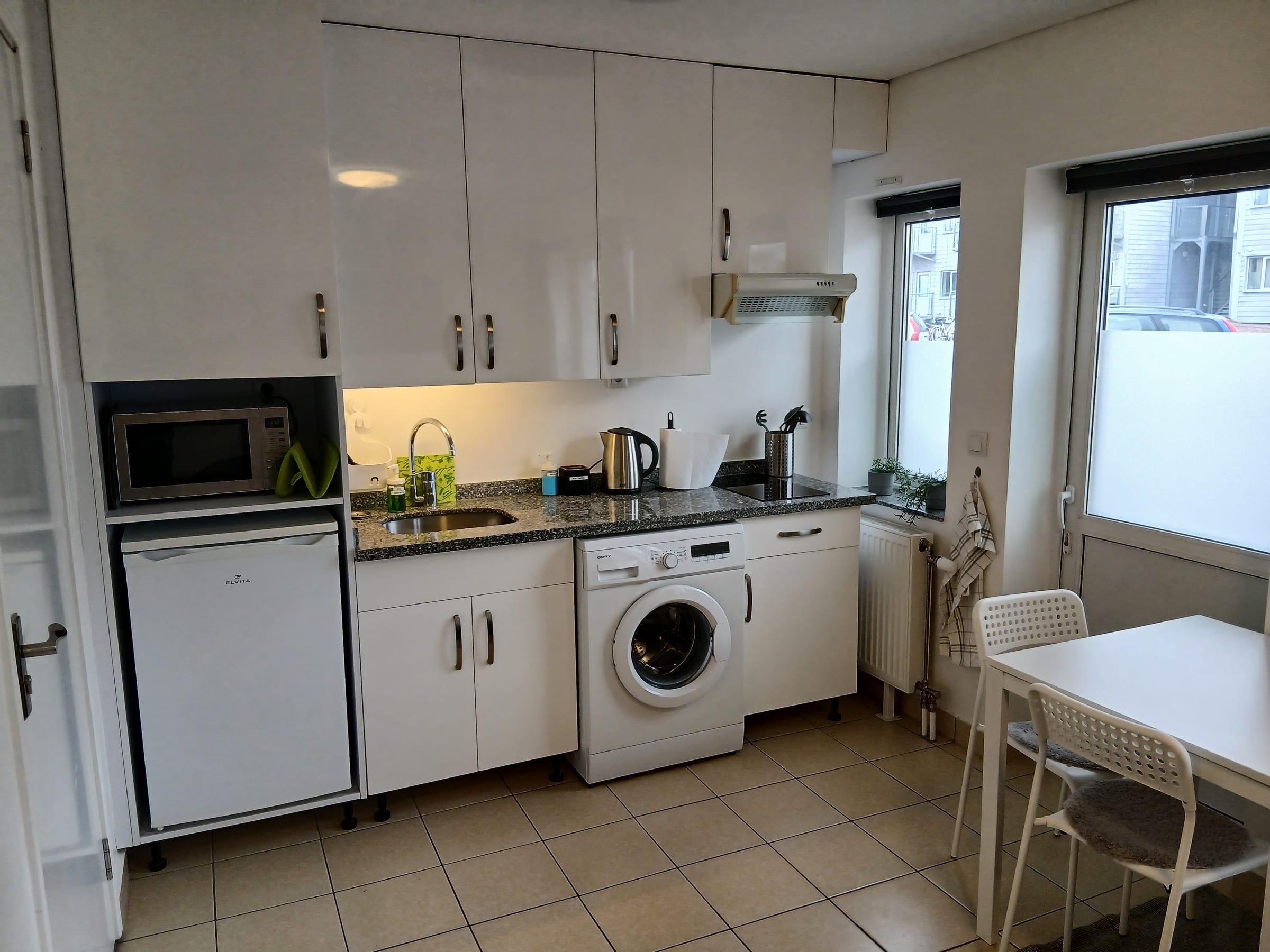 Kök med spishäll, kyl, mikrovågsugn, tvättmaskin och matplats vid fönstret