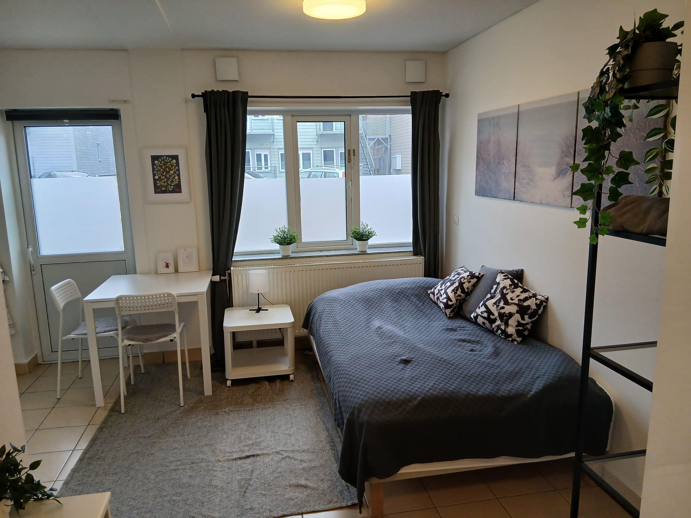 Lägenhetens sovplats med bäddad dubbelsäng, matbord och utgång mot balkongen